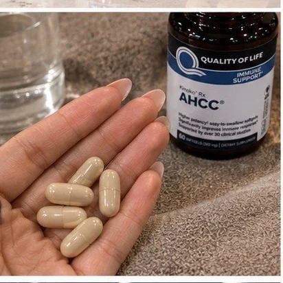 Capsules molles d’AHCC dans la paume d’une main, avec un verre d’eau et le flacon en arrière-plan
